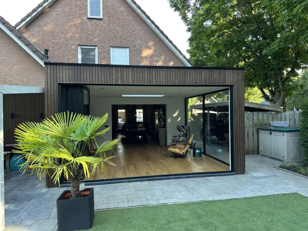 Houtskelet aanbouw met geopende harmonicapui en bamboe gevelbekleding in Susteren