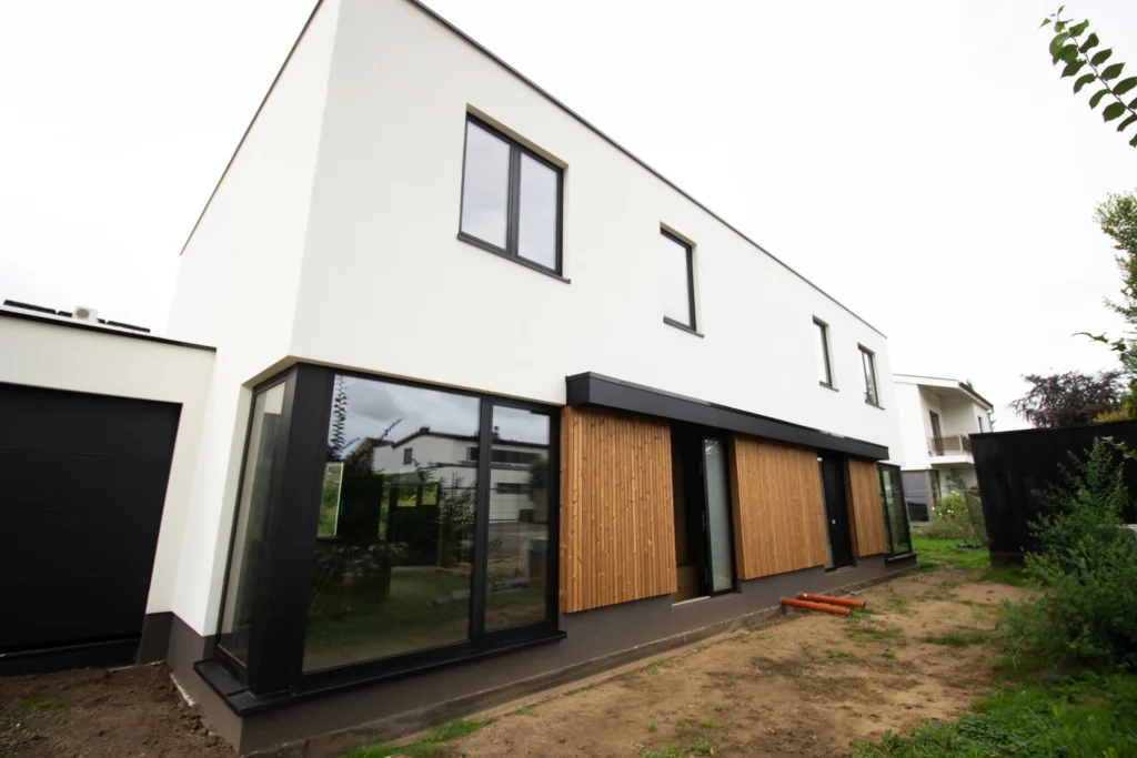 Nieuwbouw houtskeletwoning in Maaseik met witte crepi-gevel, houten gevelbekleding en aluminium kozijnen