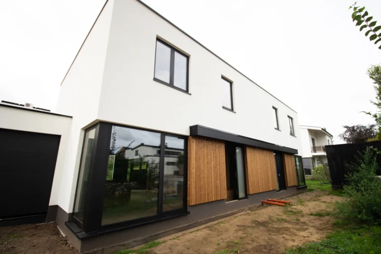 Nieuwbouw houtskeletwoning in Maaseik met witte crepi-gevel, houten gevelbekleding en aluminium kozijnen
